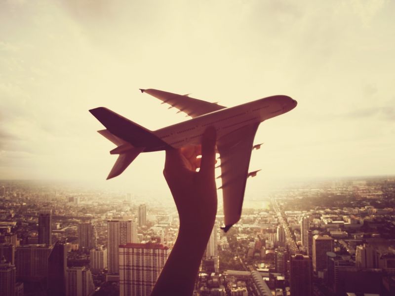 Mão de uma pessoa segurando um avião em miniatura com uma cidade ao fundo