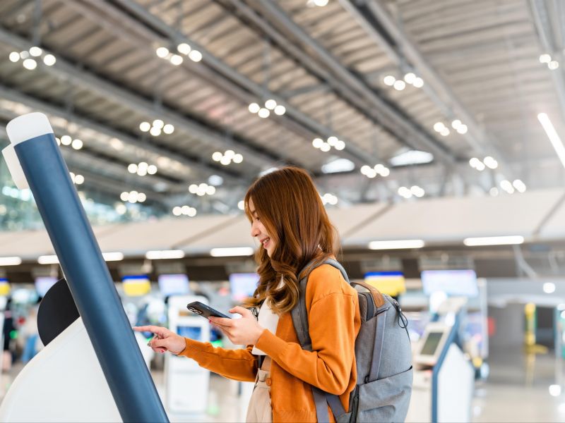 Mulher fazendo checkin usando o cartão de embarque eletrônico em um toten de atendimento