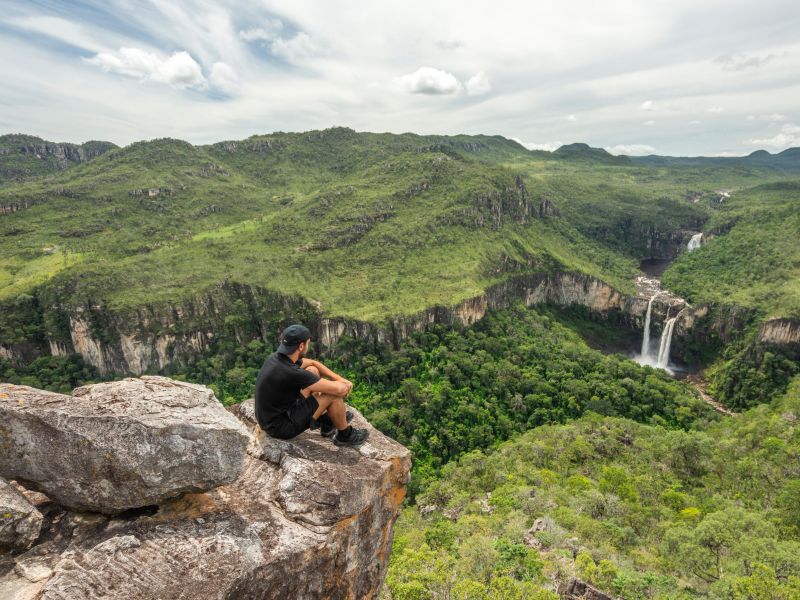 Homem sentado de pernas cruzadas na ponta de uma pedra, em um mirante na Chapada dos Veadeiros